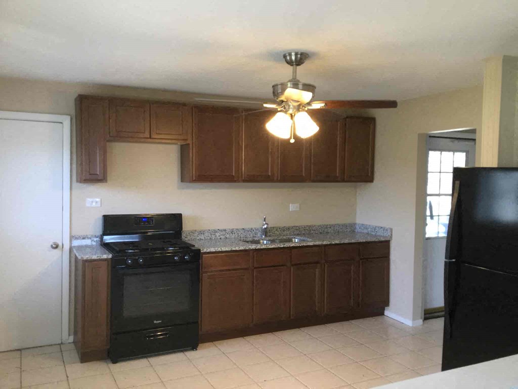 A kitchen with a black stove top oven and brown cabinets.