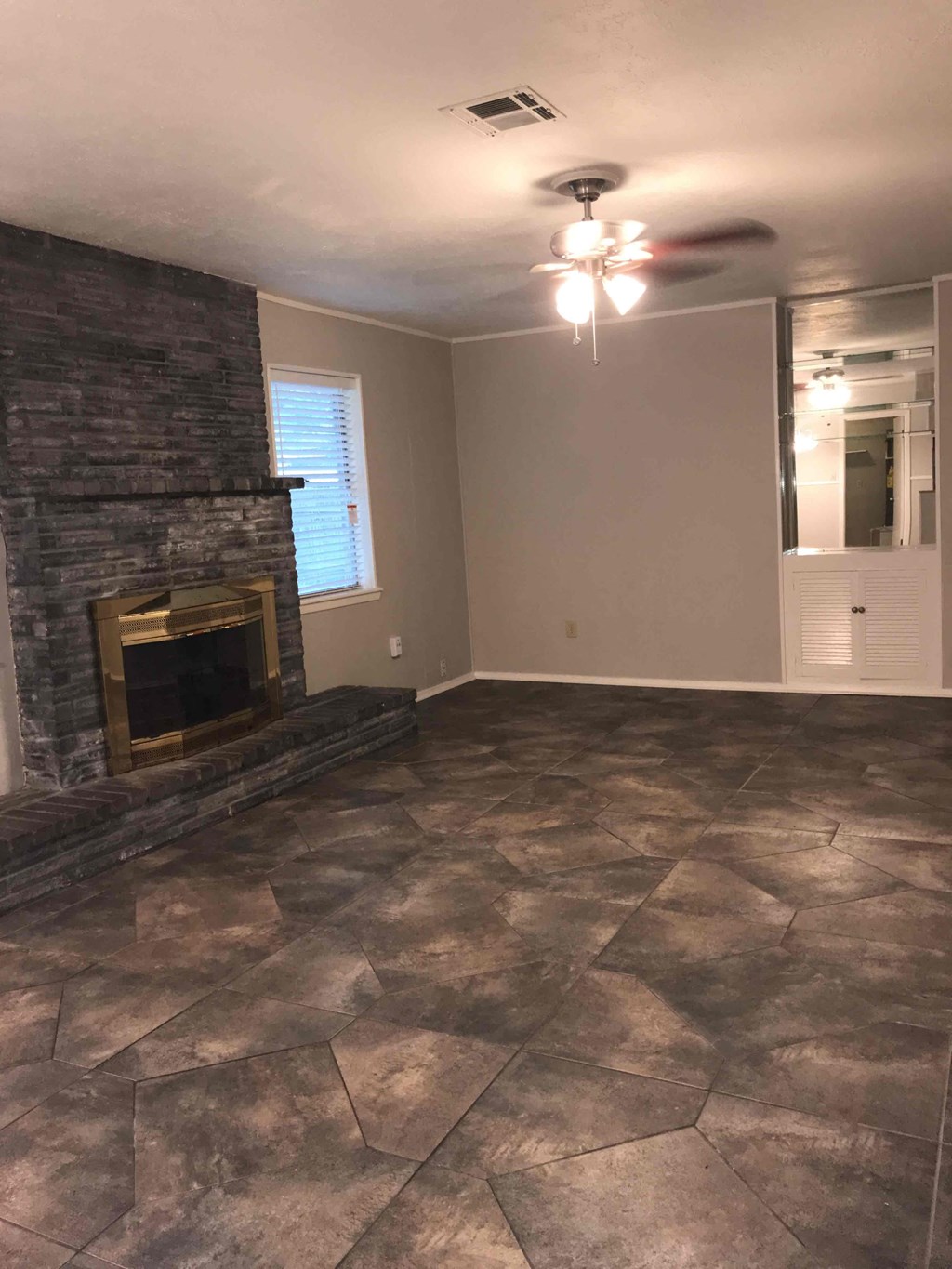 A room with a stone fireplace and a ceiling fan.
