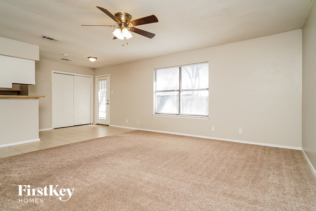 an empty living room with a ceiling fan and a kitchen