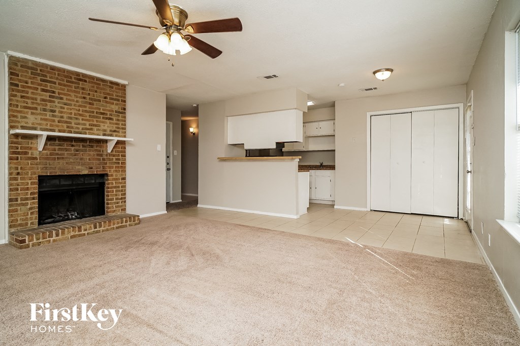 an empty living room with a brick fireplace and a ceiling fan