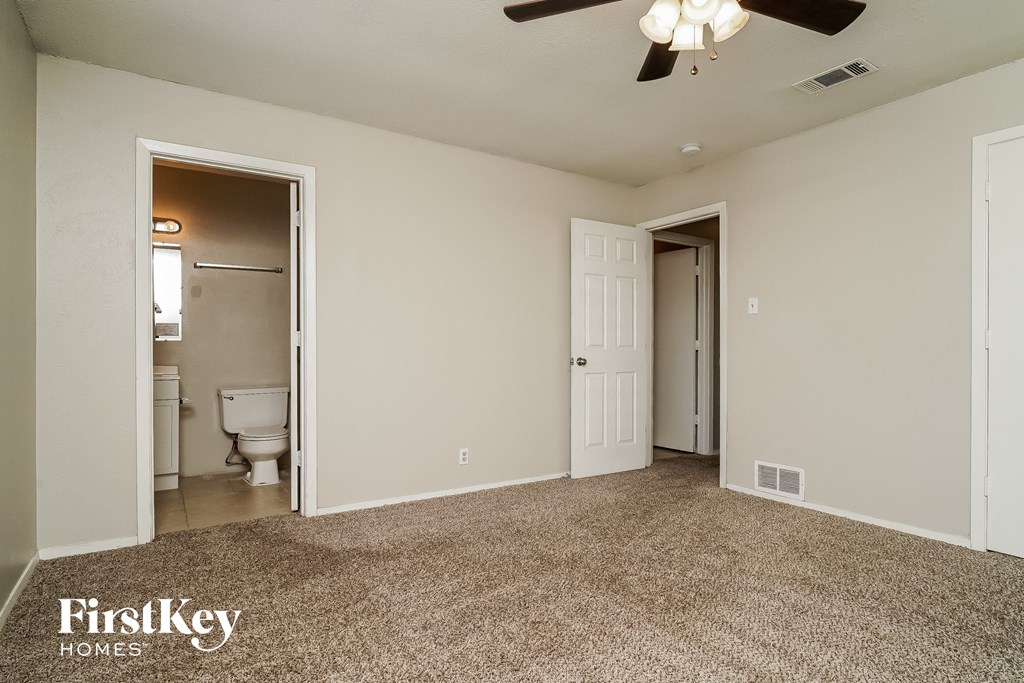 an empty living room with a ceiling fan and a door to a bathroom