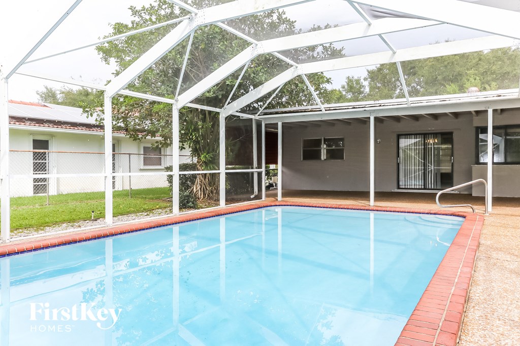 A pool under a white canopy with a house in the background.
