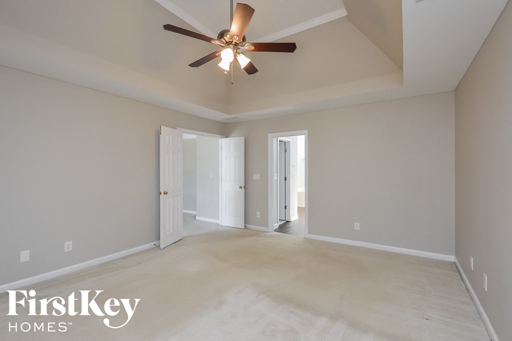 A spacious room with a ceiling fan and three doors.