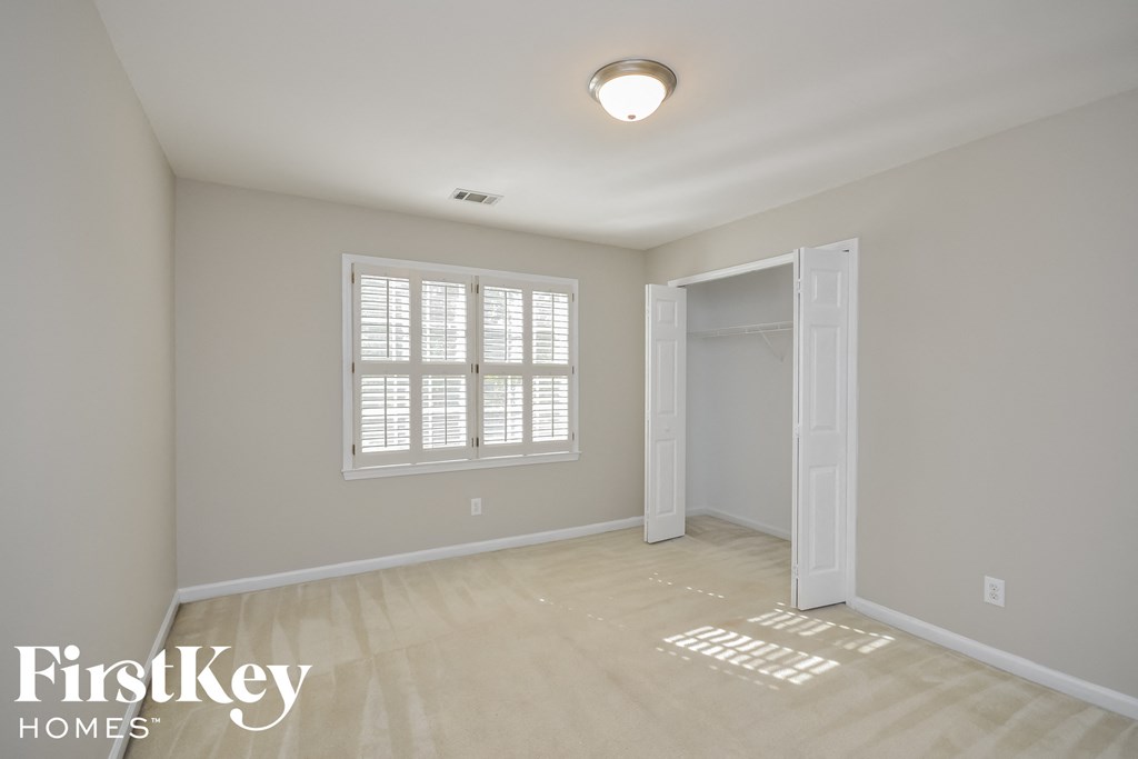 A room with a white door, a window with blinds, and a light on the ceiling.