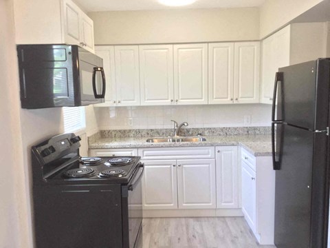 A black microwave is mounted above a black stove in a kitchen with white cabinets.