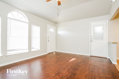 A room with wooden floors and white walls, with a ceiling fan and two doors.