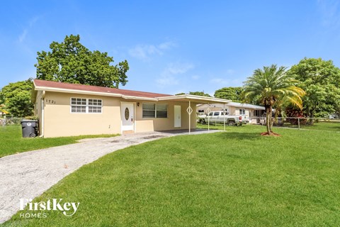 a small yellow house with a yard and a palm tree
