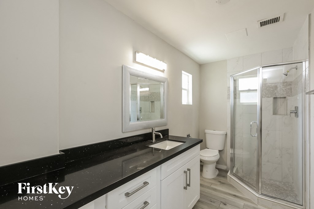 a white bathroom with a black counter top and a shower