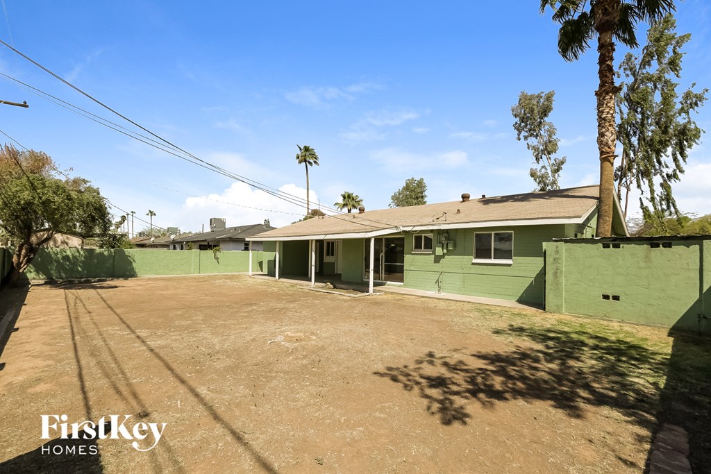 a green house with a dirt lot and palm trees