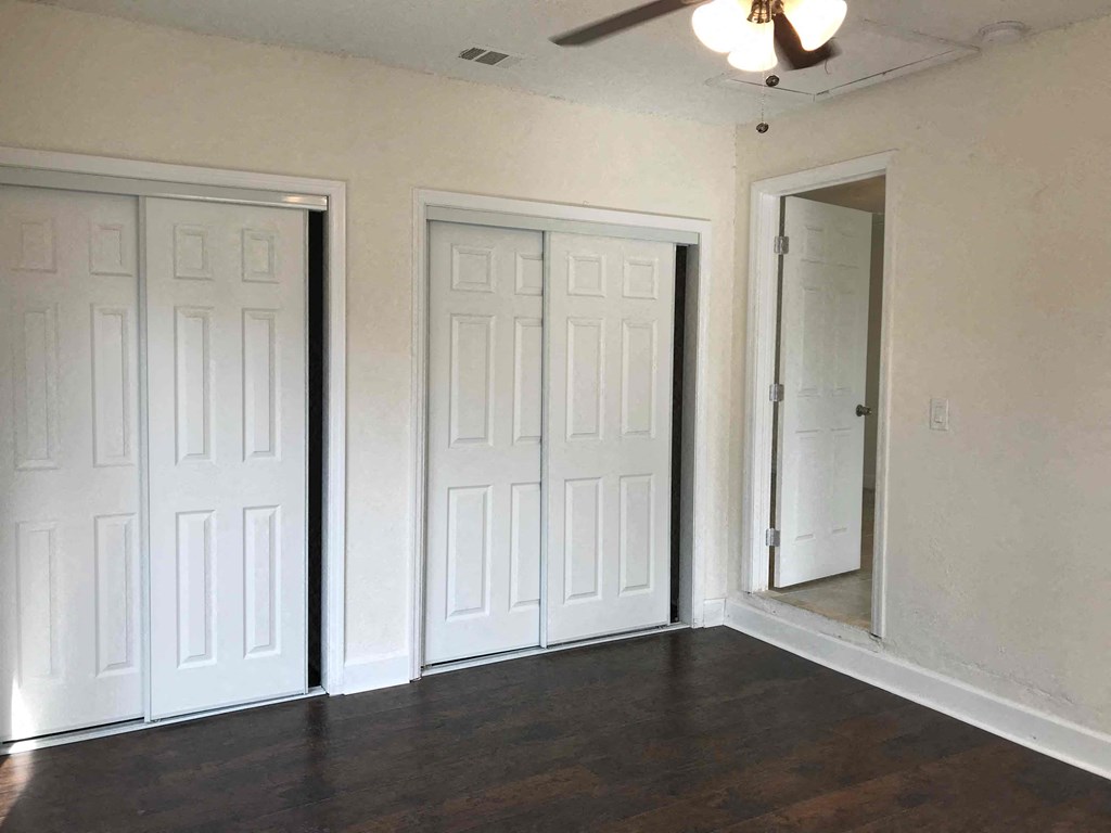 Three white doors in a room with wood floors and a ceiling fan.