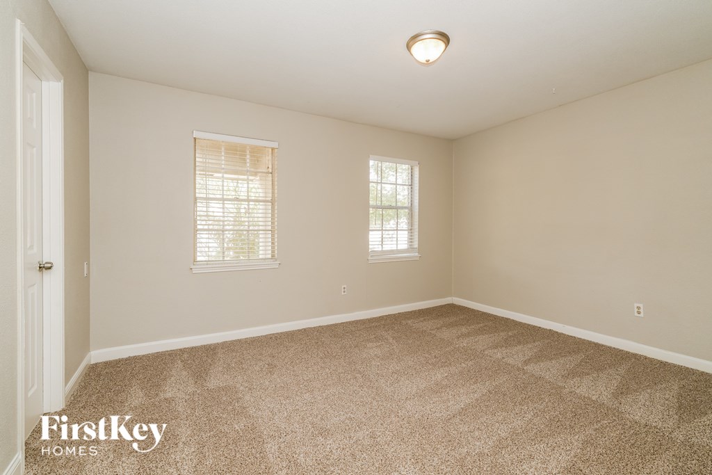 A room with a carpeted floor and two windows.