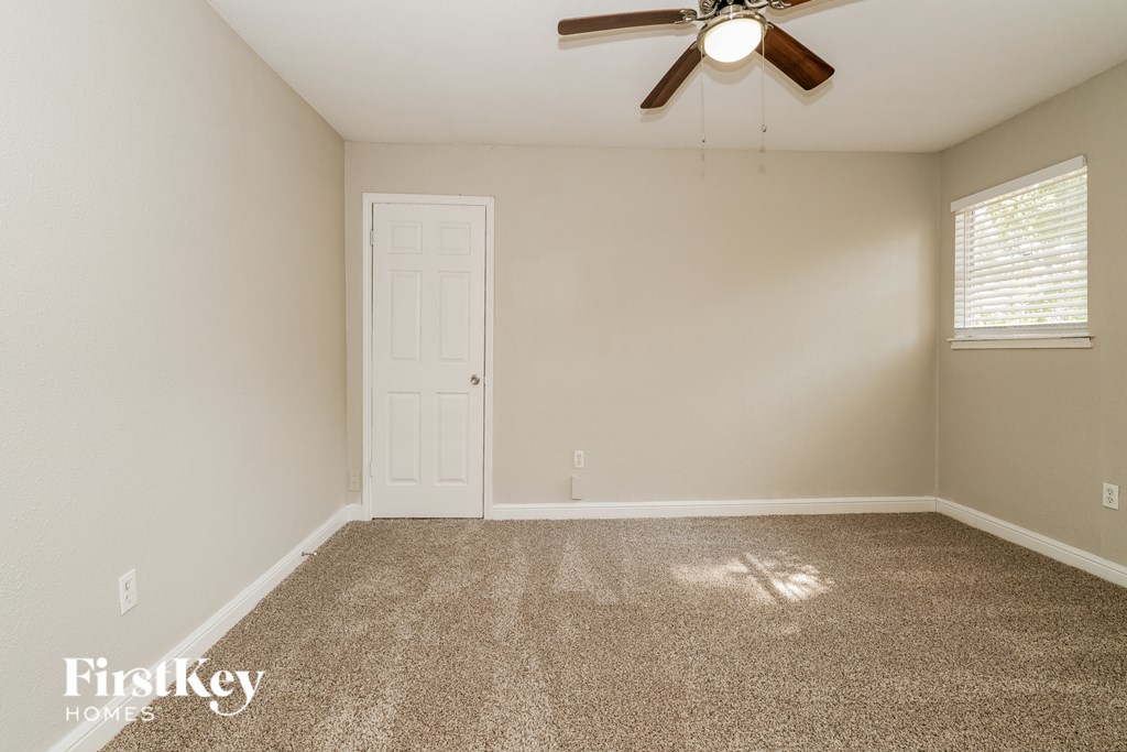A room with a carpeted floor, a ceiling fan, and a door.