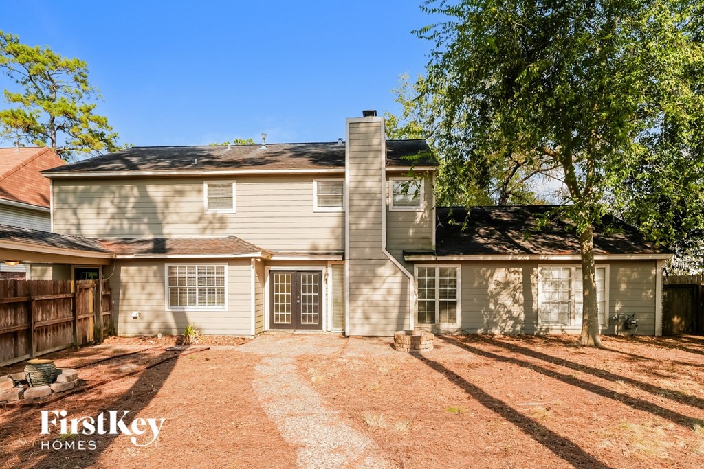 A house with a brown roof and a grey exterior is surrounded by trees and has a gravel driveway.