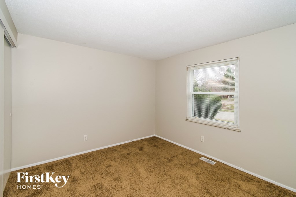 the living room of a small white house with brown carpet and a window