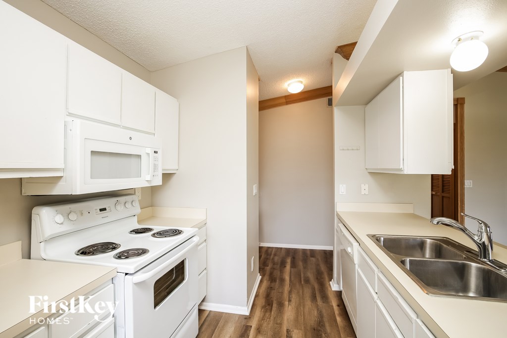 A kitchen with white appliances and wooden floors.