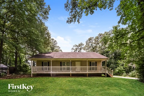 a yellow house with a wraparound porch and a yard with trees