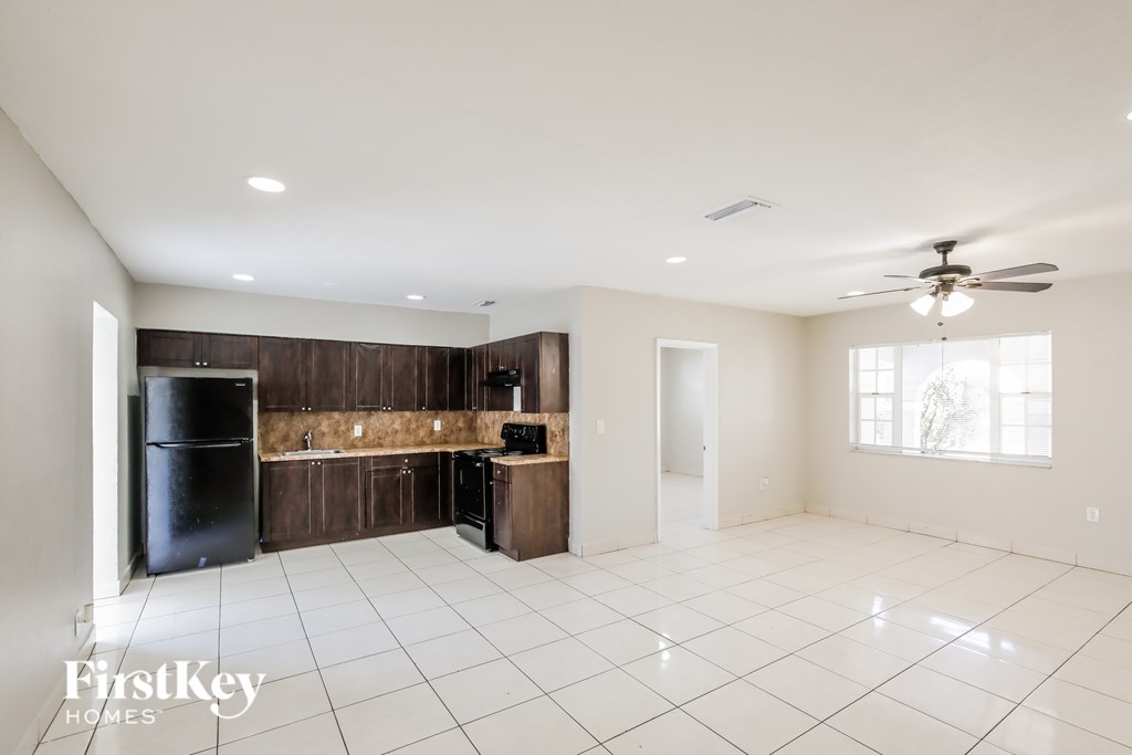 A spacious, empty room with a black refrigerator and a ceiling fan.