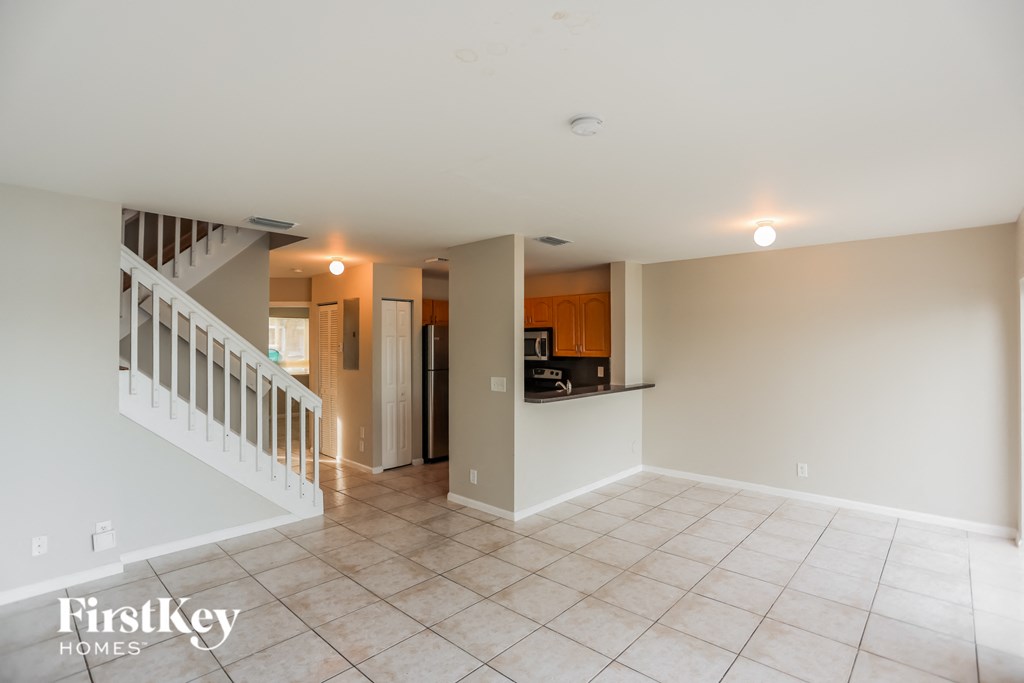 an empty living room with a staircase and a kitchen