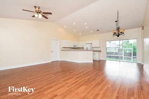 an empty living room with a kitchen and a ceiling fan