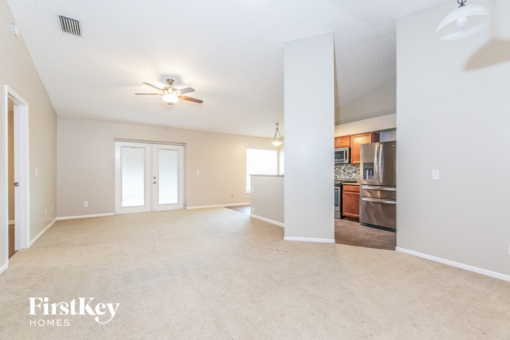 an empty living room with a ceiling fan and a kitchen