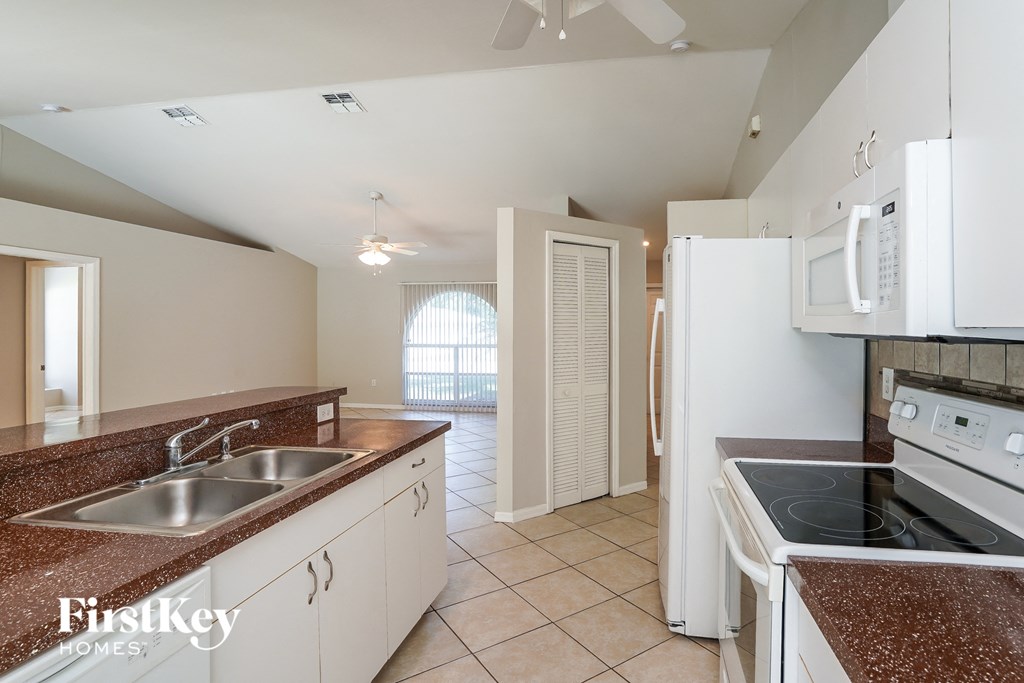 A kitchen with white appliances and brown granite countertops.