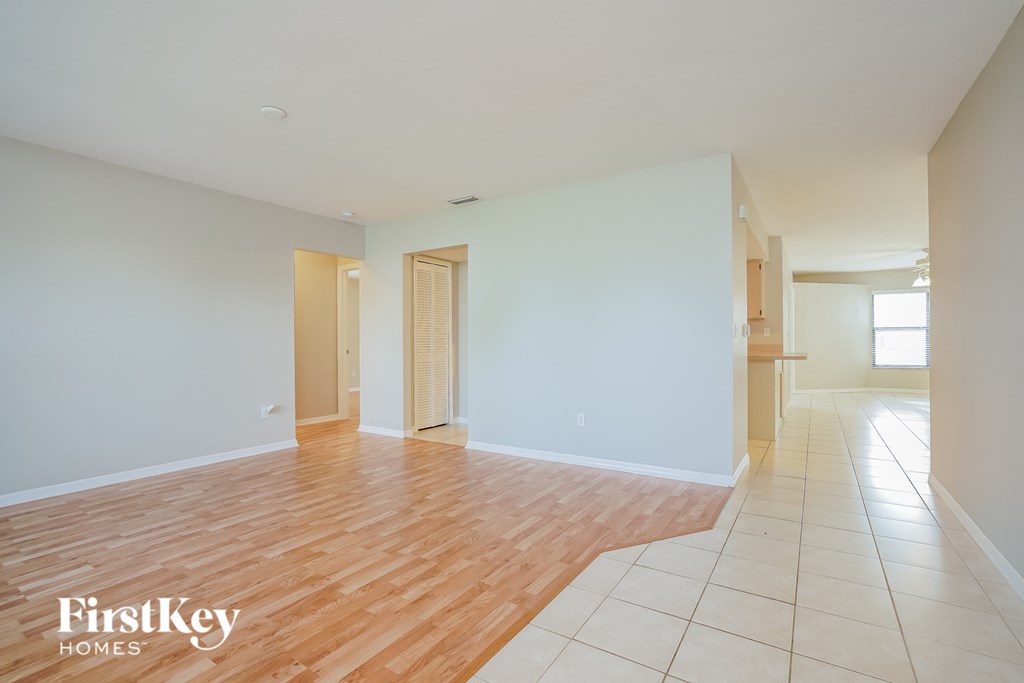 A room with wooden floors and white walls, with a door on the left and a window on the right.