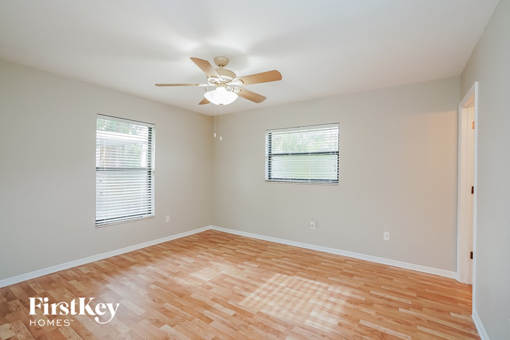A room with a ceiling fan and two windows.