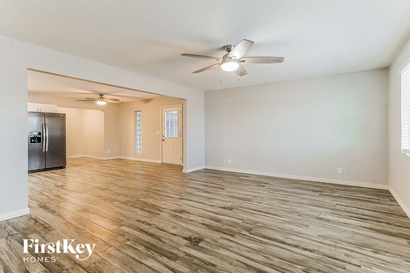 an empty living room with a ceiling fan and a refrigerator