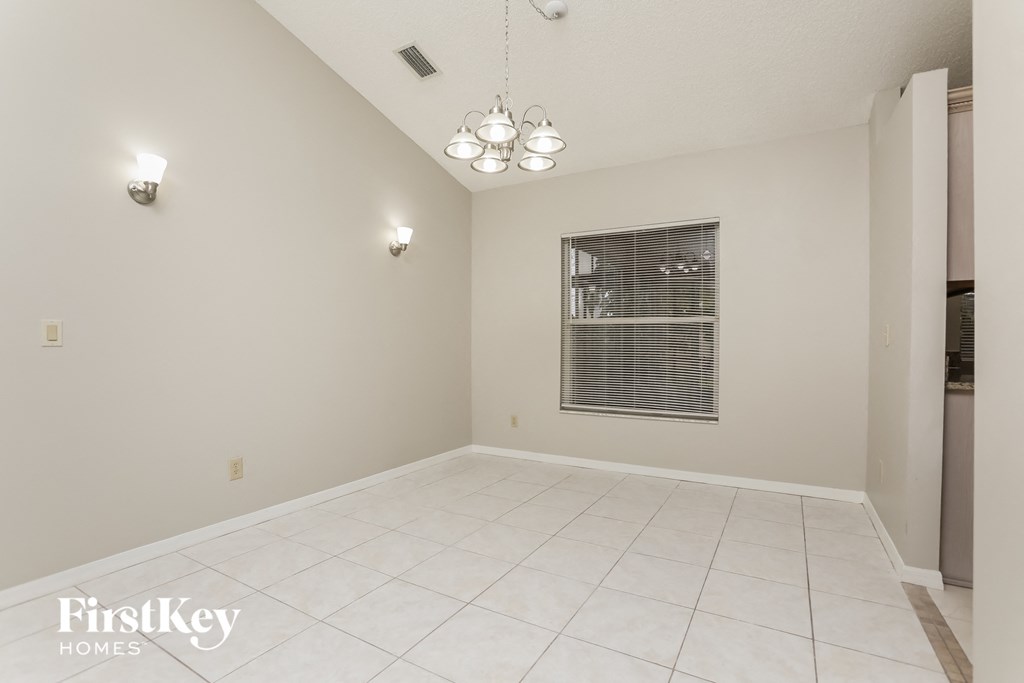 A spacious room with a chandelier and a window with blinds.