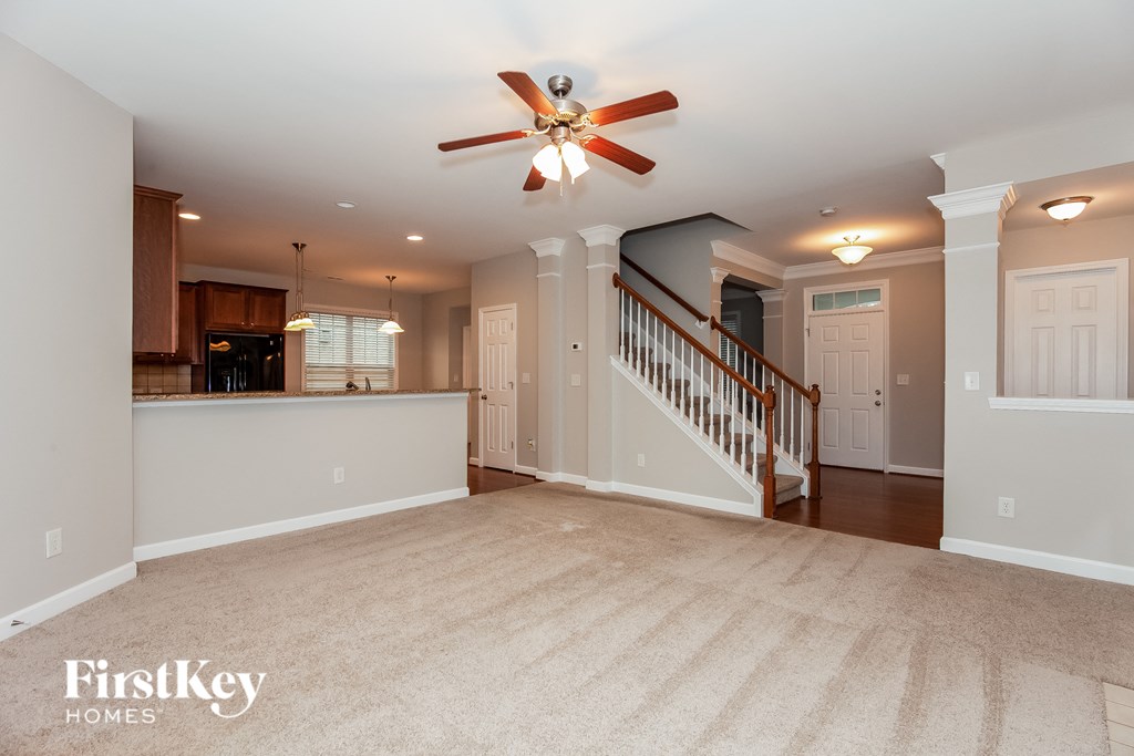 an empty living room with a kitchen and a ceiling fan