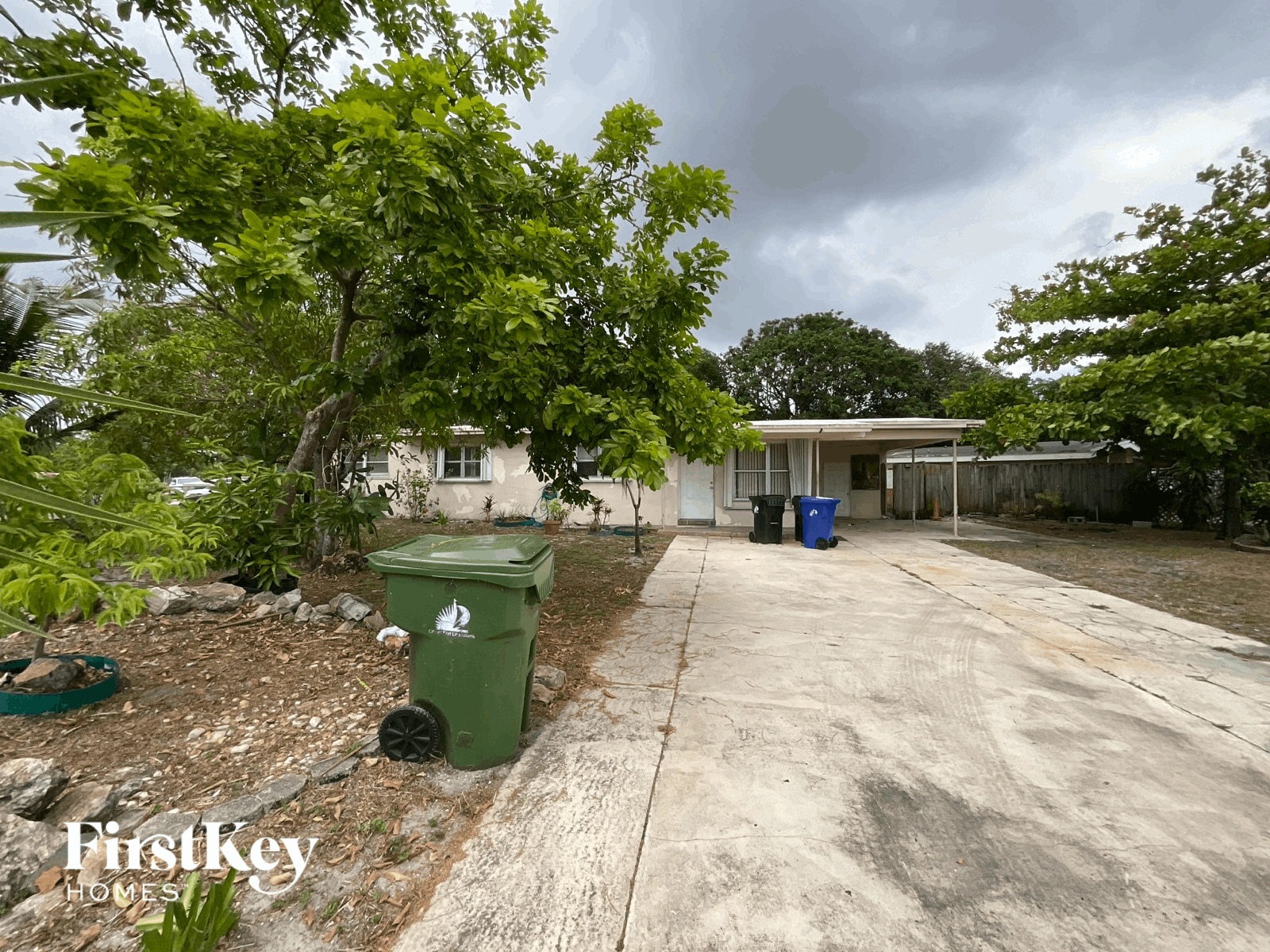 A green trash can sits on a concrete driveway.