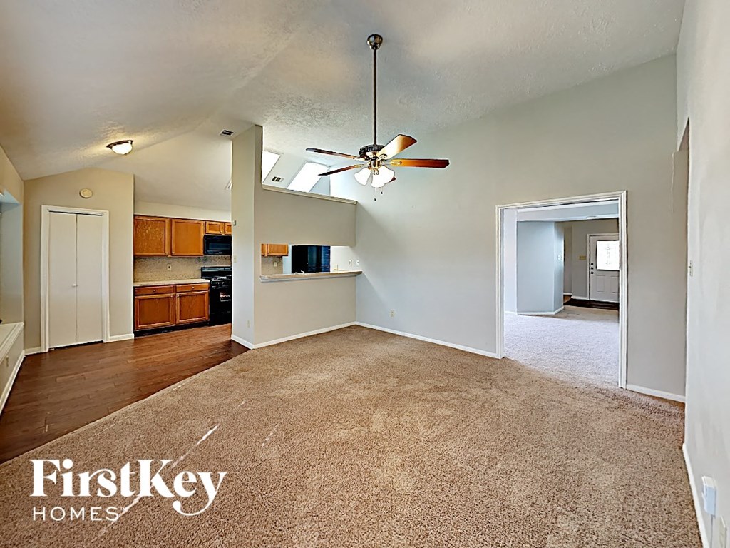 an empty living room with a ceiling fan and a kitchen