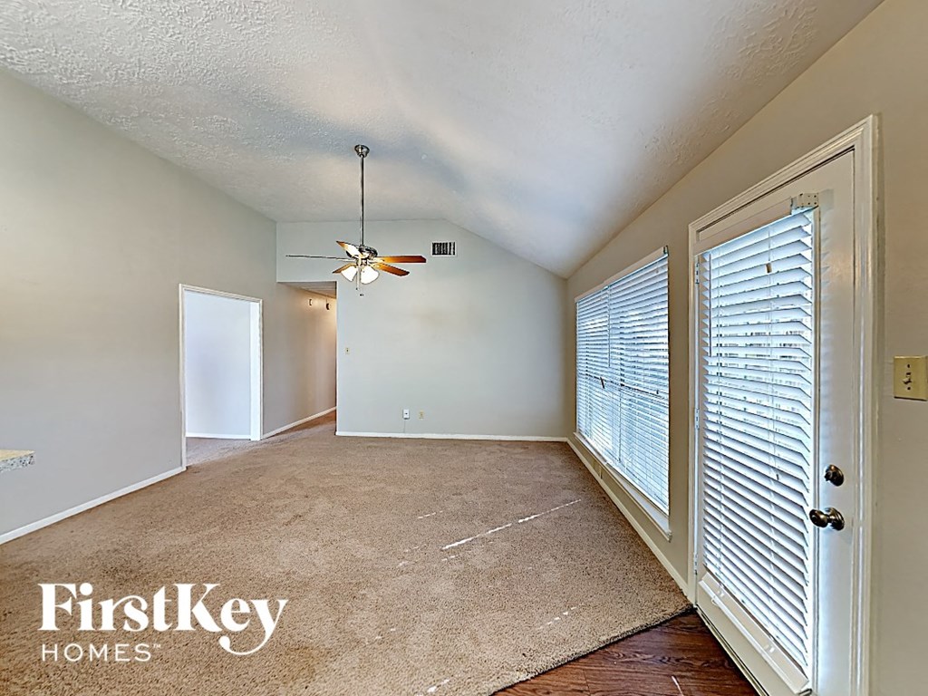 an empty living room with a large window and a ceiling fan