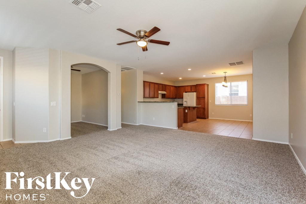an empty living room with a ceiling fan and a kitchen