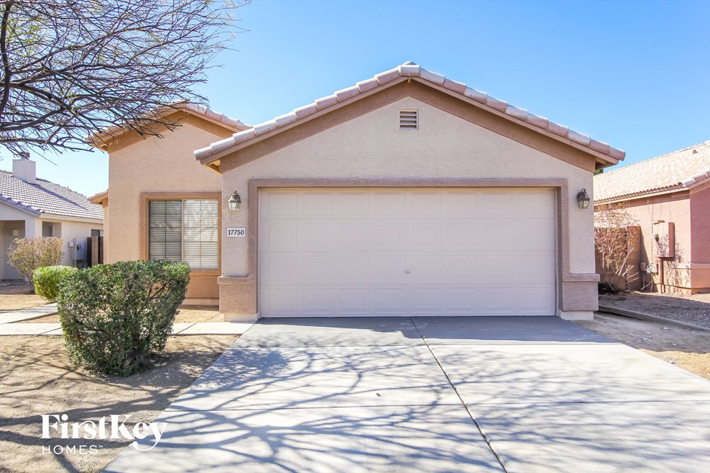 A beige house with a garage door and a tree in the front yard.