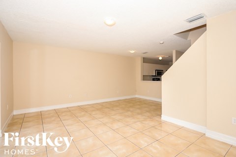A spacious room with beige walls and tiled flooring, with a FirstKey Homes logo in the corner.