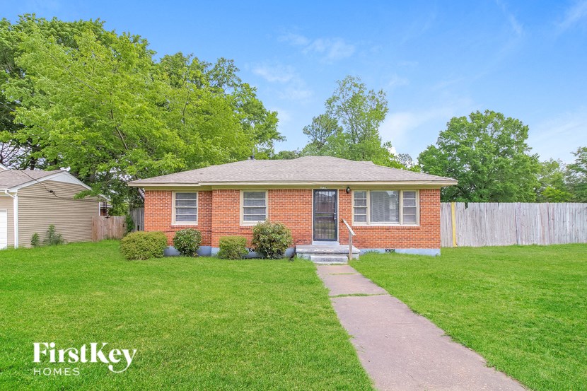 A brick house with a porch and a fence in front of it.