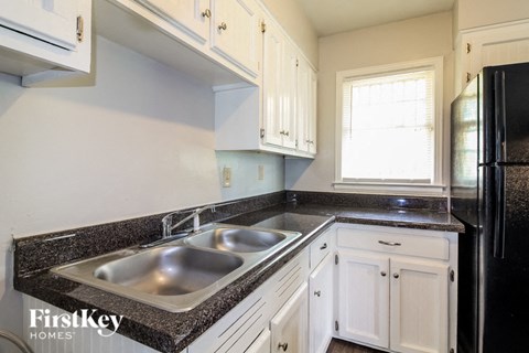 A kitchen with a black fridge and a sink with a granite counter top.