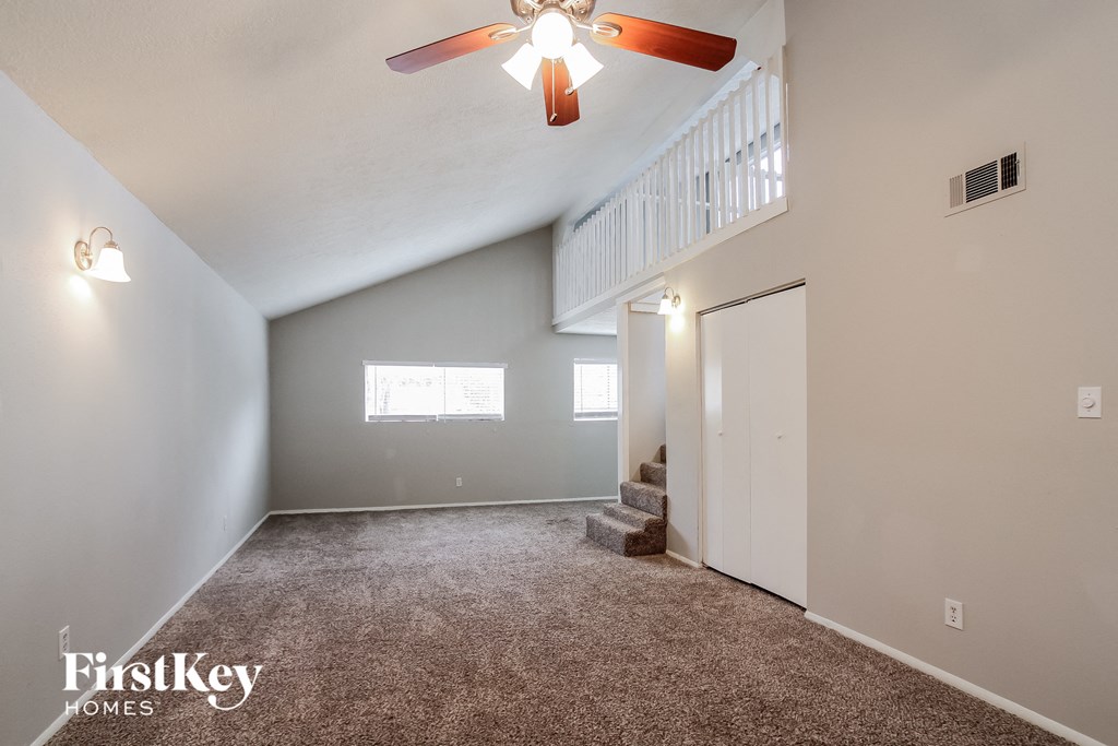 A spacious room with a carpeted floor, a ceiling fan, and a staircase leading to another room.
