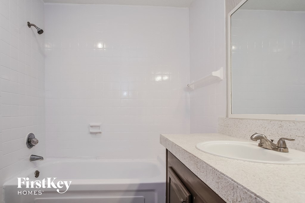 A white bathroom with a tub, sink and mirror.