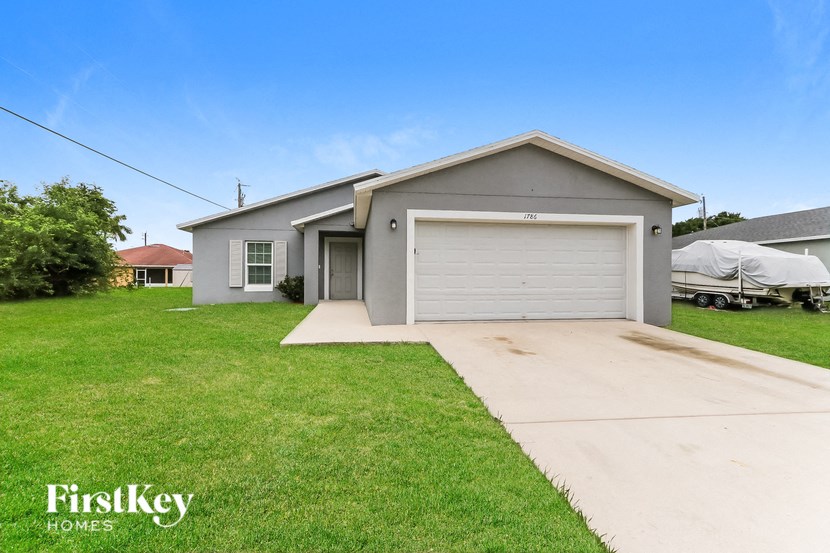 a small gray house with a driveway and a lawn
