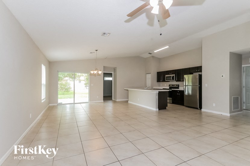 an empty living room with a kitchen and a ceiling fan