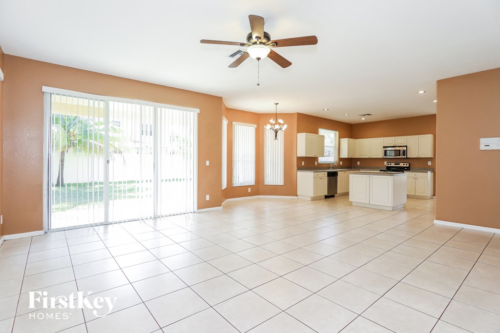 an empty living room with a kitchen and a ceiling fan