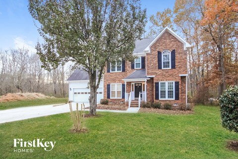 A brick house with a white door and windows is surrounded by trees.