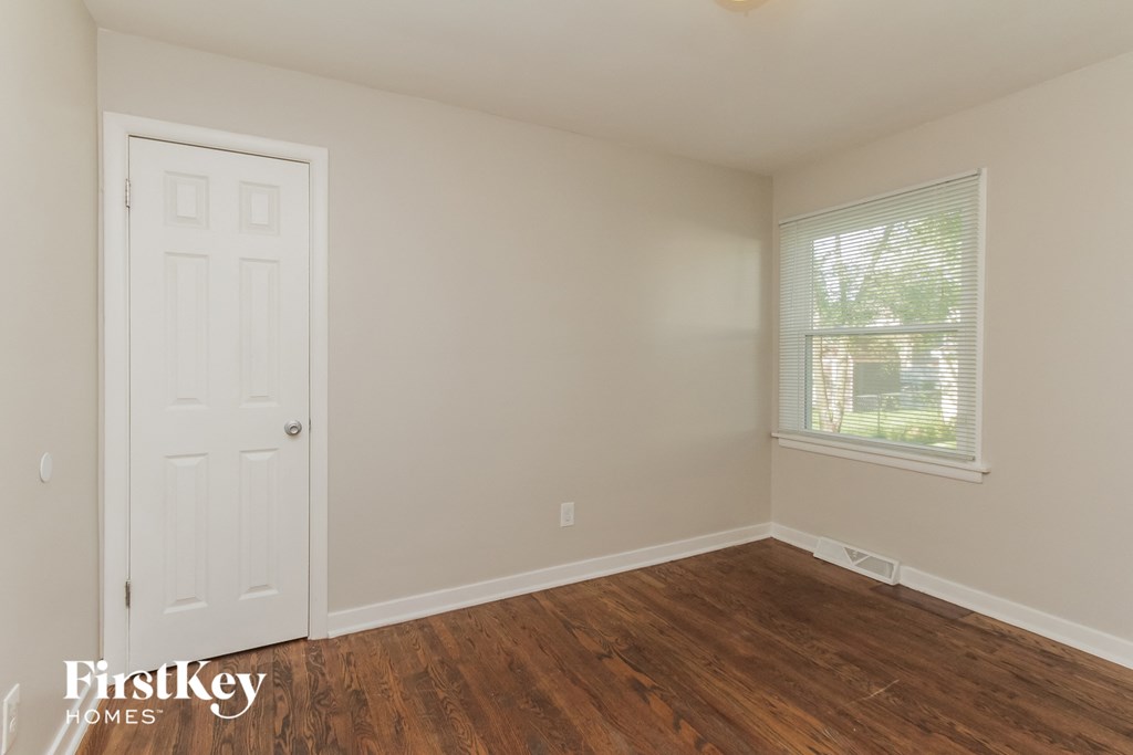 a bedroom with wooden floors and a white door and a window