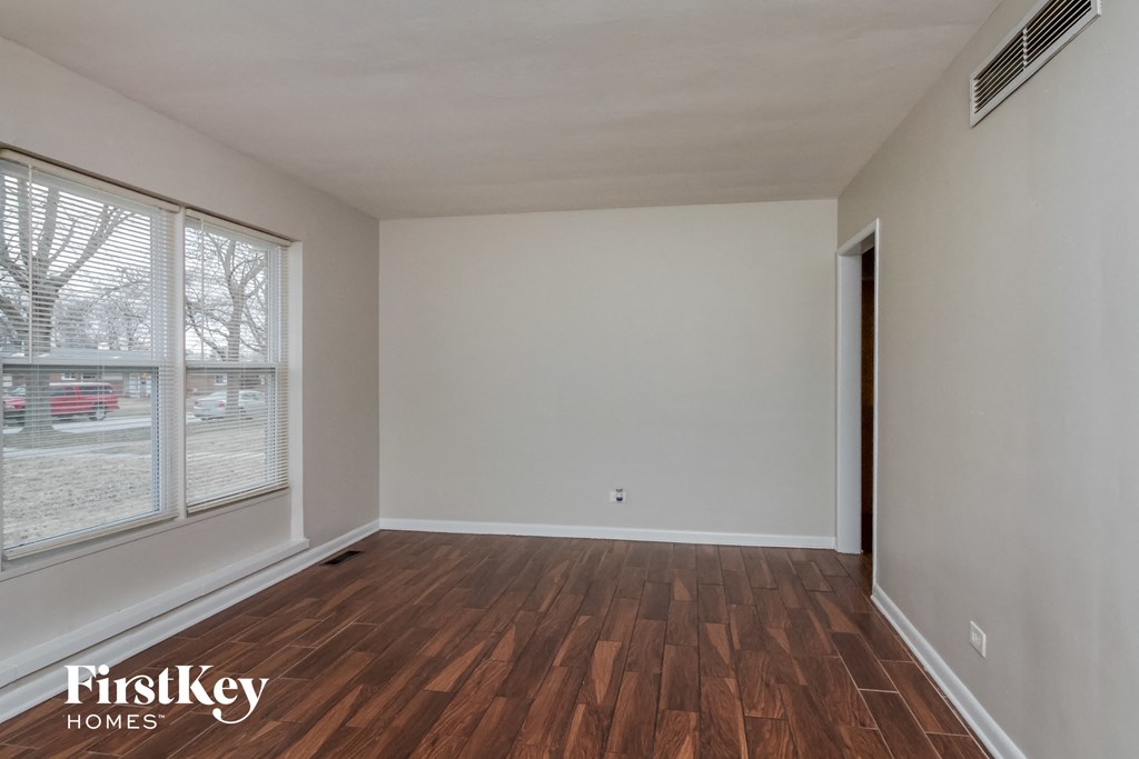 A room with wooden flooring and a window overlooking a parking lot.