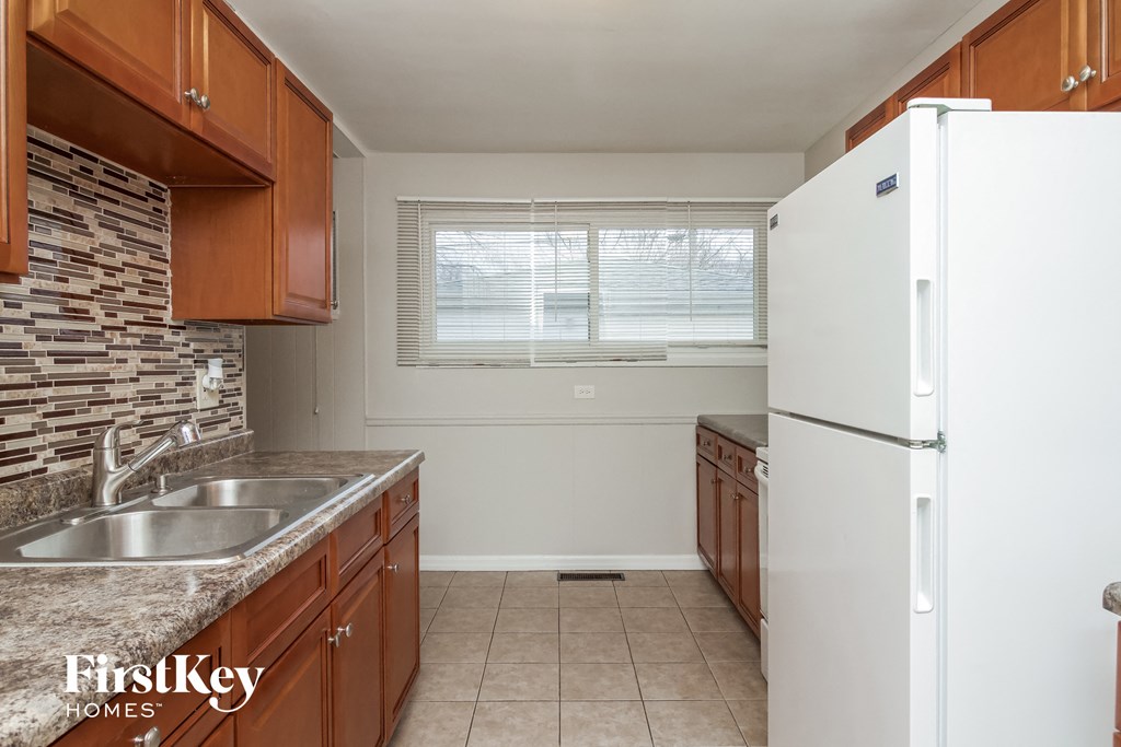 A kitchen with a white fridge, brown cabinets, and a stone backsplash.