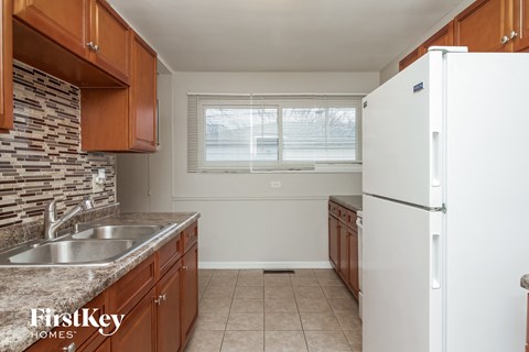 A kitchen with a white fridge, brown cabinets, and a stone backsplash.