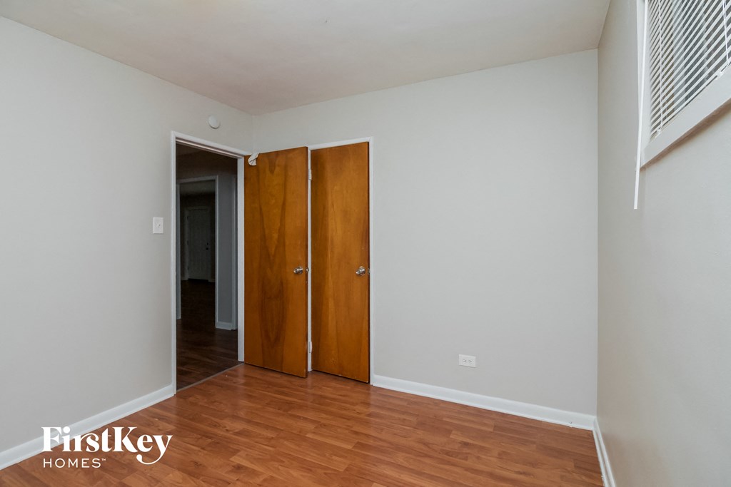 A room with a wooden floor and a white wall with a door and a window.