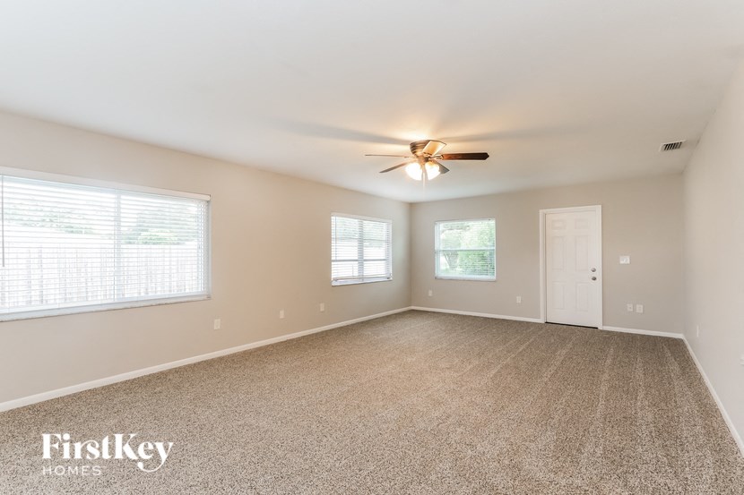 an empty living room with a ceiling fan and two windows